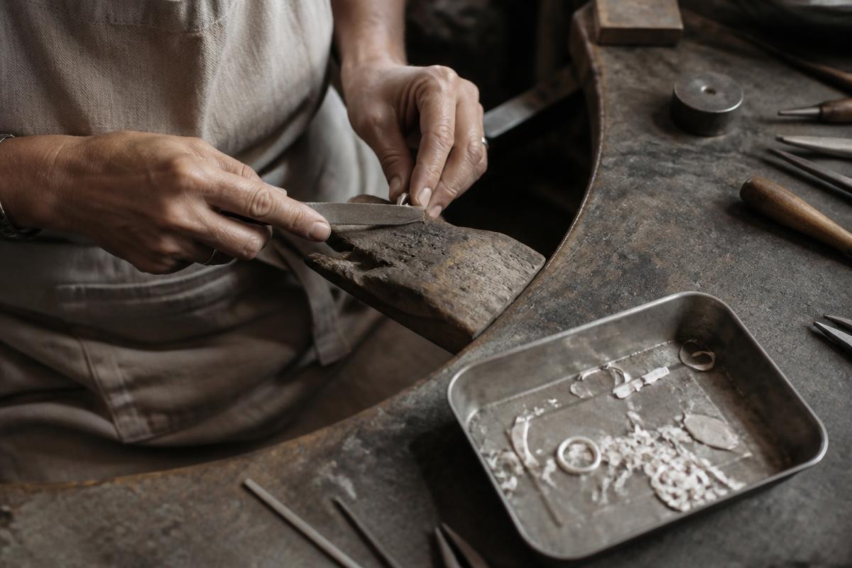 A silversmith shaping recycled silver by hand at the workbench
